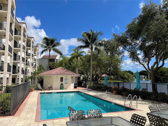 View of an apartment complex with a swimming pool and surrounding trees.