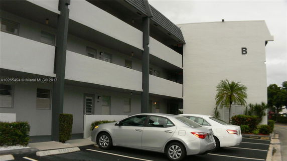 Parking area in front of a multi-story building with balconies.