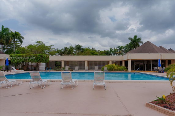 Outdoor swimming pool area with lounge chairs and a building in the background.