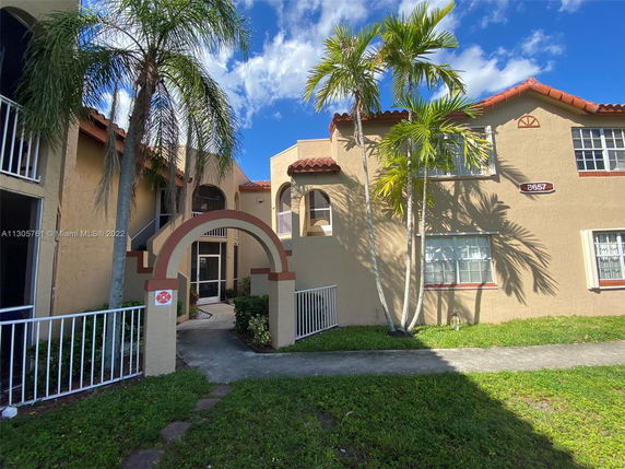 Front view of a two-story building with arched entrance and palm trees.