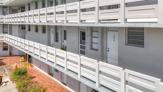 Front view of a multi-story building with white railings and numbered doors.