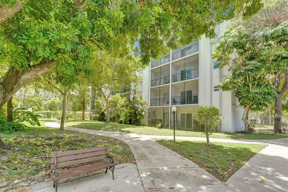 Front view of a multi-story building with balconies, surrounded by trees and a pathway.