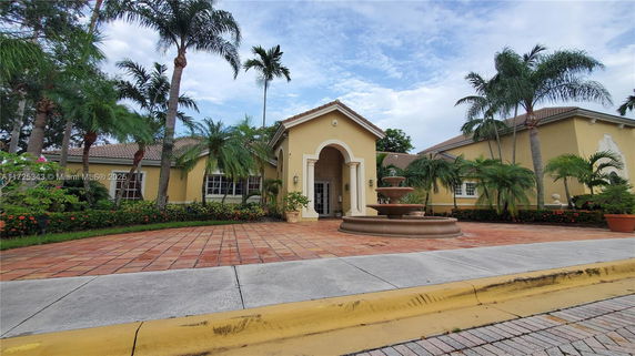 Front view of a building with a tiled roof and central entrance, surrounded by palm trees.