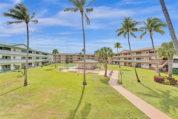 View of a residential complex with multiple three-story buildings surrounding a central courtyard with grass and palm trees.