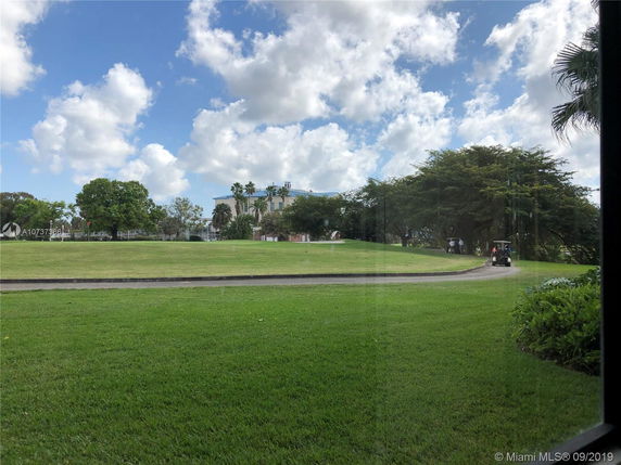 View of a golf course with a path, trees, and a building in the distance.
