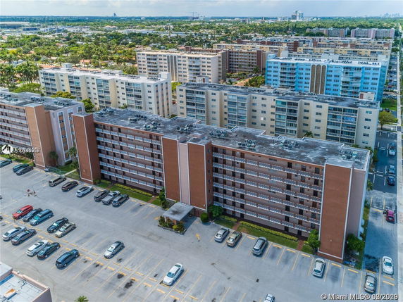 Aerial view of a multi-story apartment complex with adjacent parking lots and nearby residential buildings.