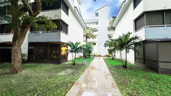 Pathway leading through a landscaped area between multi-story residential buildings.