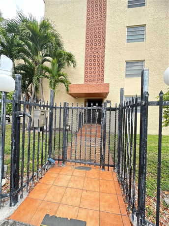 Front view of a multi-story building with a gated entrance and tiled pathway.
