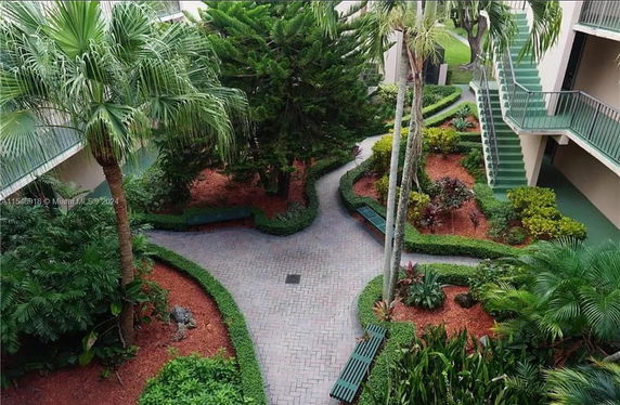 Garden area with winding pathways and benches, with adjacent apartment building stairs.