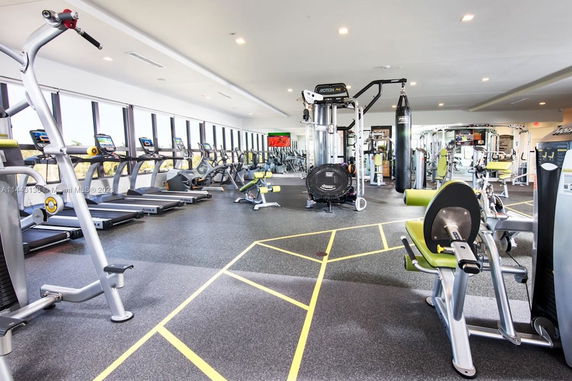 Interior view of a gym with various exercise equipment and large windows.