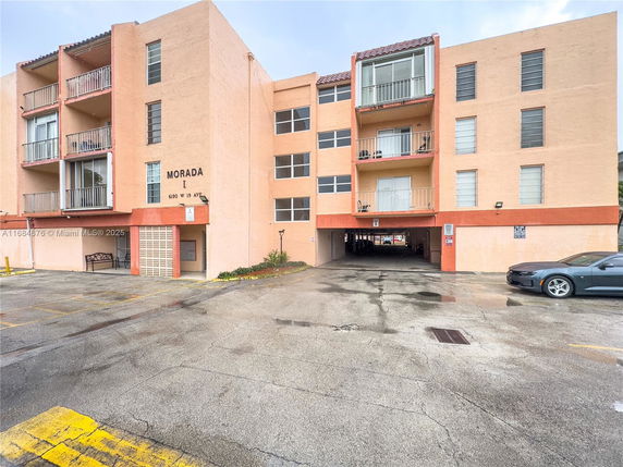 Front view of a multi-story building with balconies and a parking area.