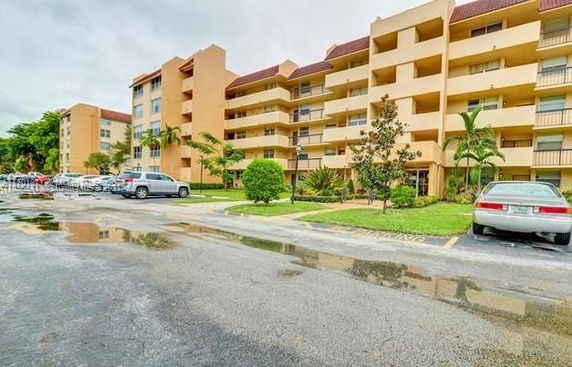 Front view of a multi-story apartment building with balconies and adjacent parking area.
