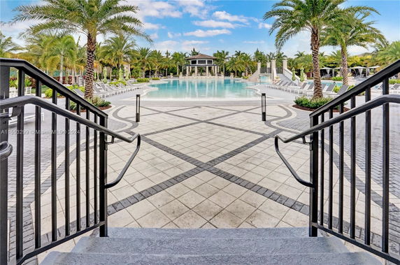 View of a large outdoor swimming pool with palm trees and poolside lounge chairs.