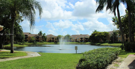 Outdoor view of a pond with a fountain, surrounded by residential buildings and trees.