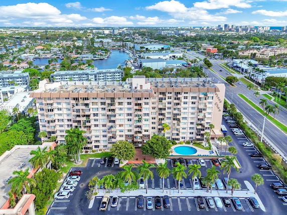 Aerial view of a multi-story building with adjacent parking area and swimming pool, surrounded by roads and other buildings.