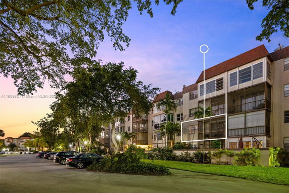 Front view of a multi-story residential building with screened balconies and a parking area.