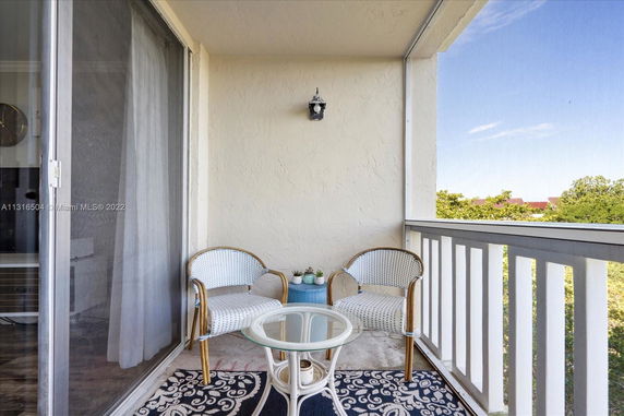 Balcony with two chairs, a small table, and a view of greenery and distant buildings.