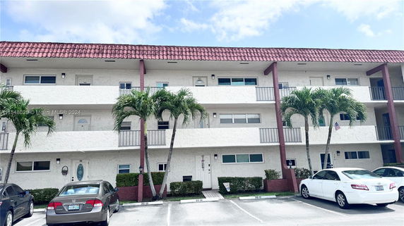 Front view of a three-story apartment building with balconies and parking area.