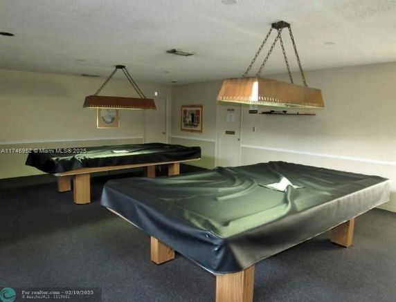 Room with two billiard tables covered with black cloths and overhead lights.
