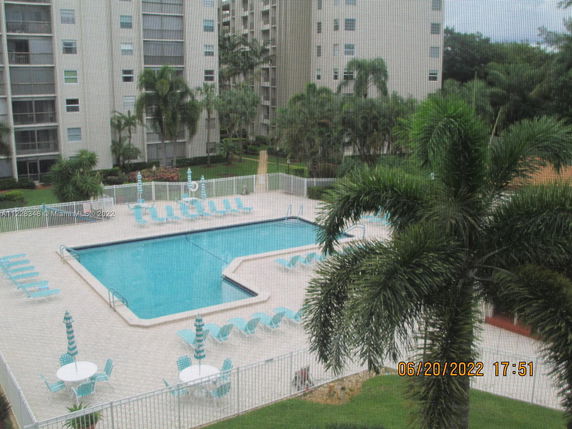 View of apartment buildings overlooking a swimming pool area with patio furniture and palm trees.