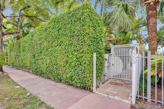 View of a tall hedge and a gated entrance on a sidewalk.