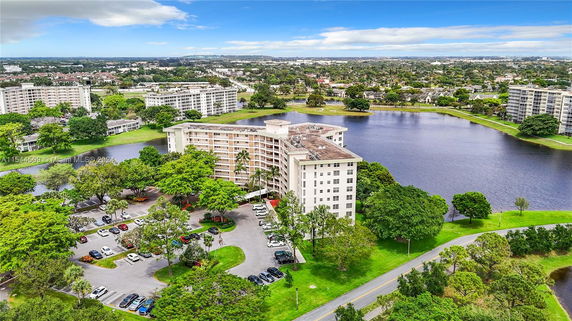 Aerial view of apartment buildings surrounded by trees and a body of water.