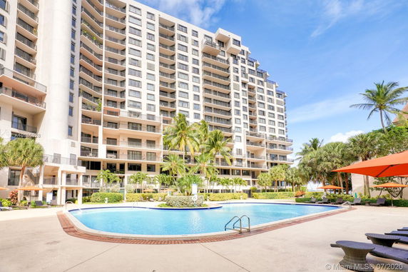 Front view of a multi-story residential building with balconies and a pool in the foreground.
