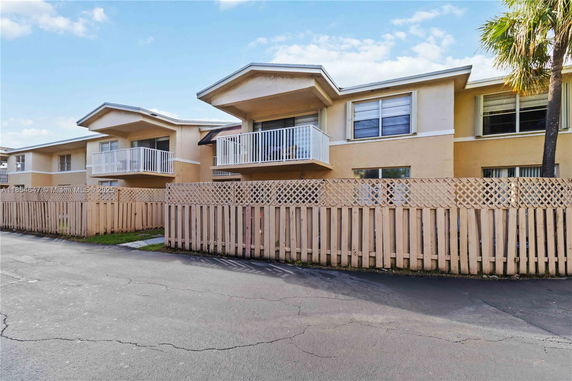 Front view of a two-story building with balconies and a wooden fence.