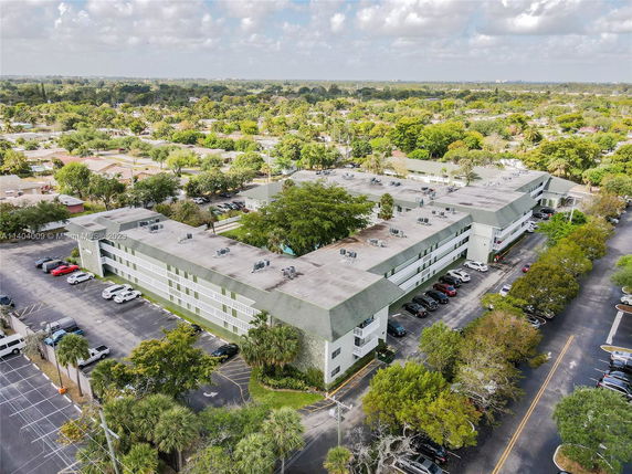 Aerial view of a multi-story building complex surrounded by a parking lot and greenery.