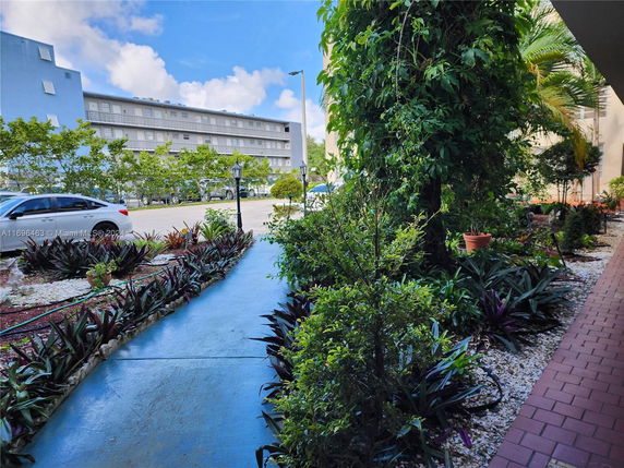 Outdoor parking area near a building with greenery and parked cars.