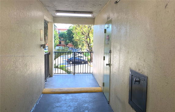 Corridor leading to a view of a parking area with trees and cars.