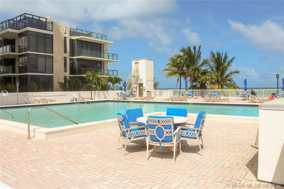 View of a modern multi-story building near a swimming pool with outdoor seating.