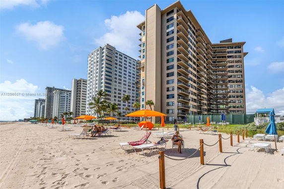 View of beachfront high-rise buildings with sandy beach and umbrellas in the foreground.