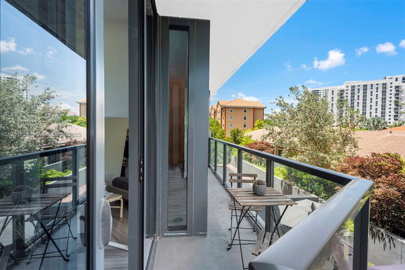 View from a balcony with a glass railing overlooking surrounding trees and buildings.