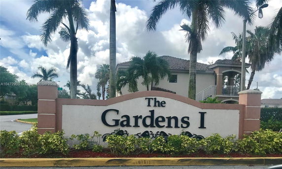 Front view of a residential building with palm trees and a sign labeled 'The Gardens I'.
