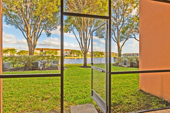View from a building's screen enclosure showing grass, trees, and a body of water.