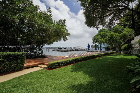 View of a waterfront area with a wooden deck, sun loungers, and boats docked nearby.