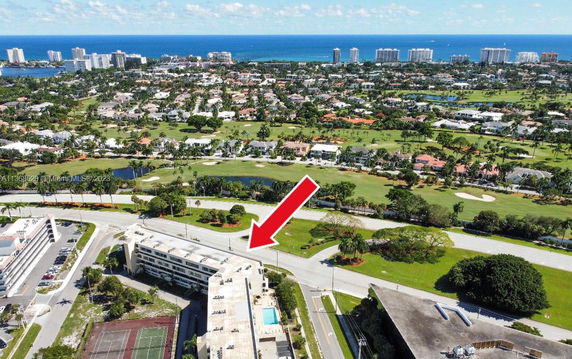 Aerial view of a building and its adjacent tennis courts with a golf course and ocean in the background.