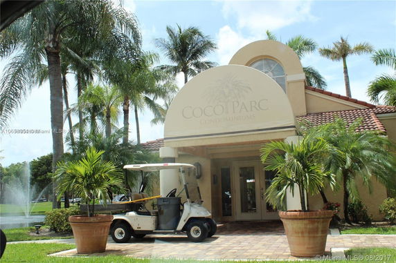 Front view of a condominium building entrance with decorative plants and a golf cart.