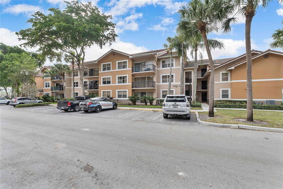Exterior view of a multi-story apartment building with a parking area in front.