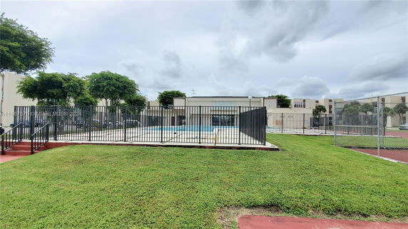 Outdoor area with a fenced swimming pool and surrounding green lawn.