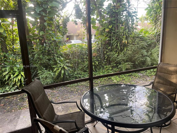View of a patio area with a glass table and chairs, overlooking lush greenery.