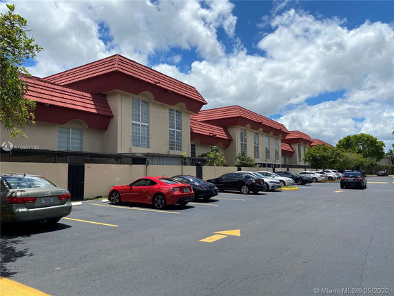 Parking area in front of a building with red-tiled roof and multiple vehicles.