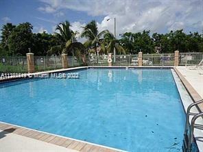 Outdoor swimming pool with a fence and palm trees in the background.
