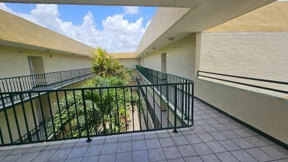 View of a building corridor with railings and greenery below.