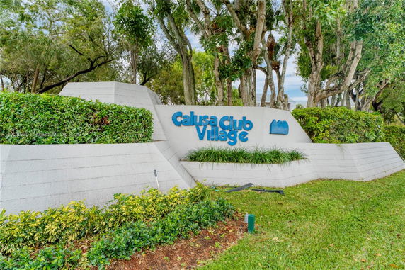 Entrance sign for Calusa Club Village surrounded by greenery.
