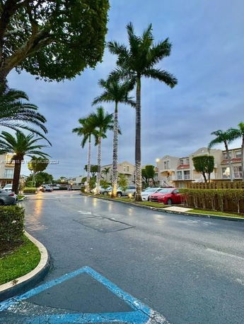 View of residential buildings lined with palm trees and parked cars.