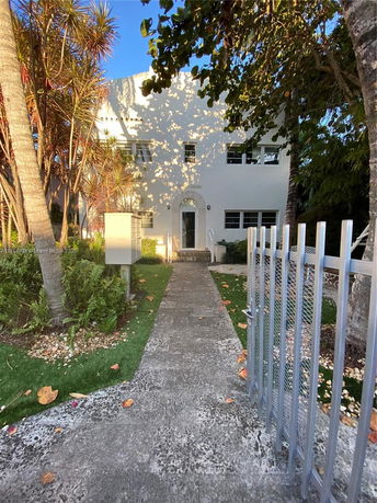 Front view of a two-story house with a white façade and gated entrance.