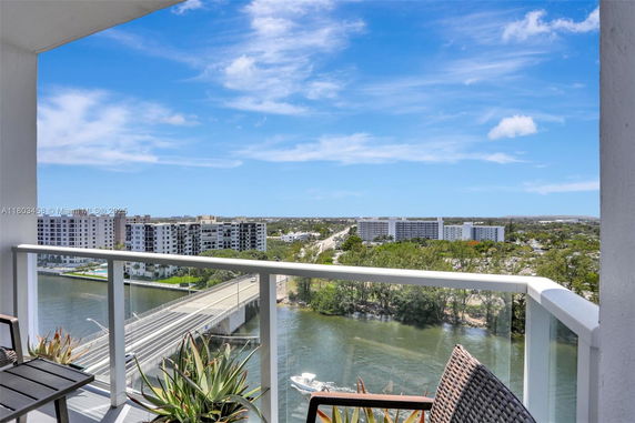 View from a building balcony overlooking a road, water body, and distant buildings.