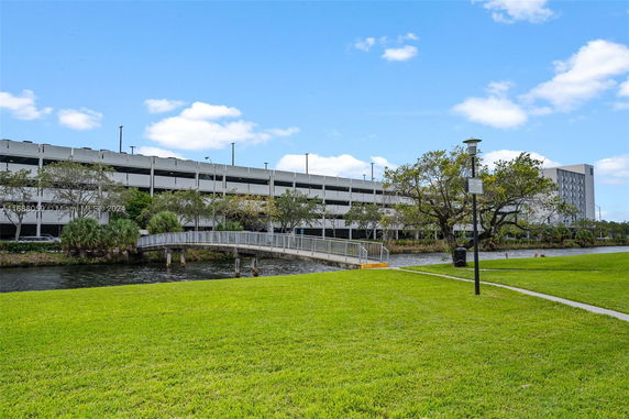 View of a multi-level parking structure near a waterway with green lawn and trees in the foreground.